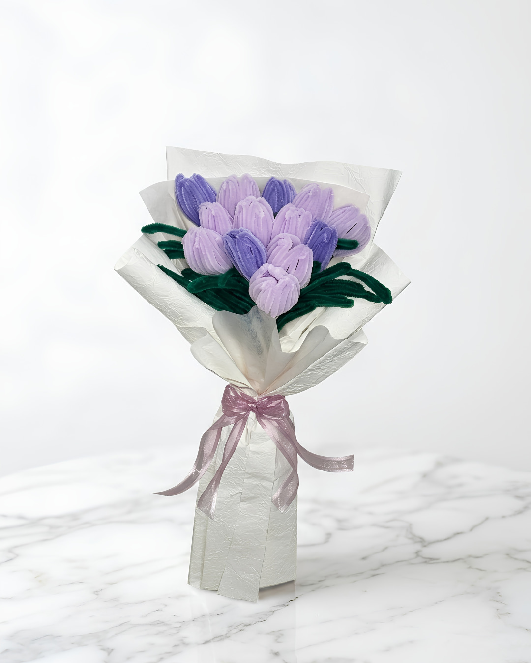 Ramo de tulipanes lilas eternos hechos a mano en chenille, envueltos en papel blanco satinado con lazo de cinta malva, sobre mármol blanco